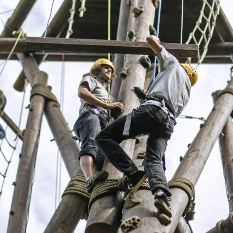 Students in harnesses climb a wooden structure