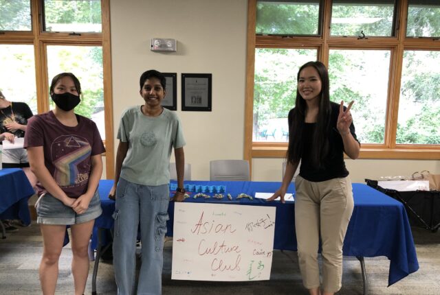 学生在亚洲文化俱乐部微笑的照片在桌子前面说“亚洲文化俱乐部”的一个标志。